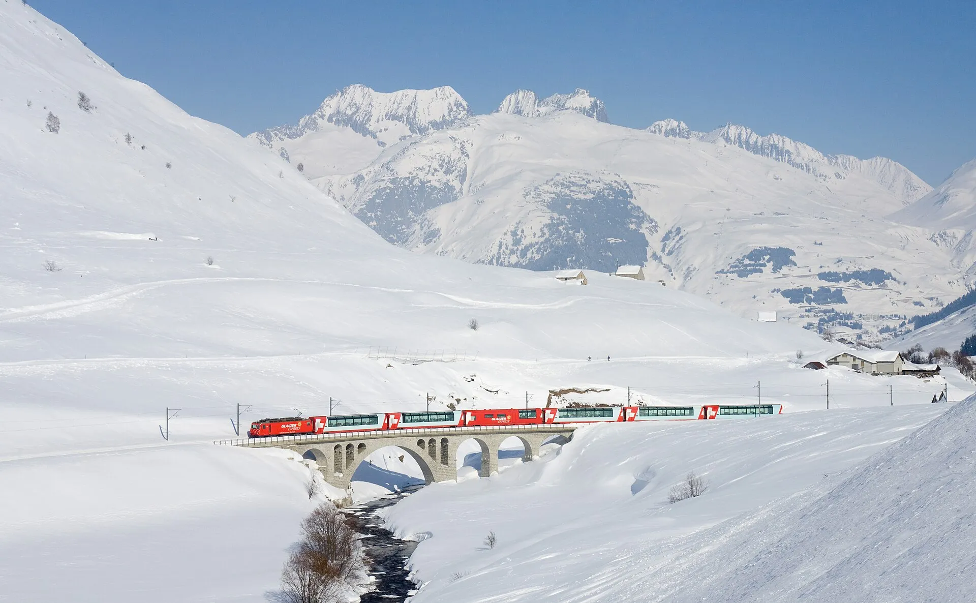 The Glacier Express crossing a stone bridge near Hospental in a snow-covered Urseren valley.