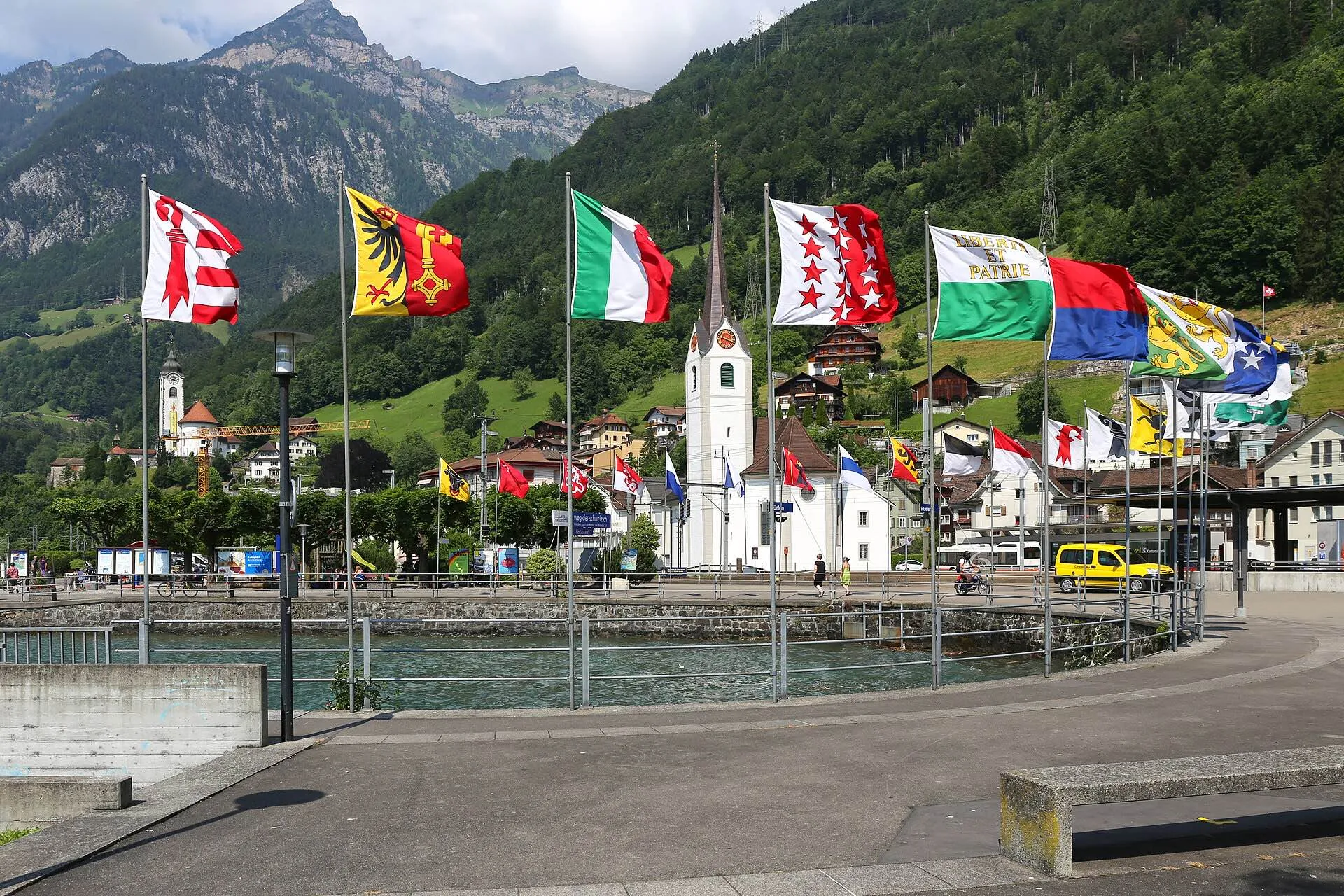 The lakeside at Flüelen, where the boat meets the train, with flags, the church and mountains behind.