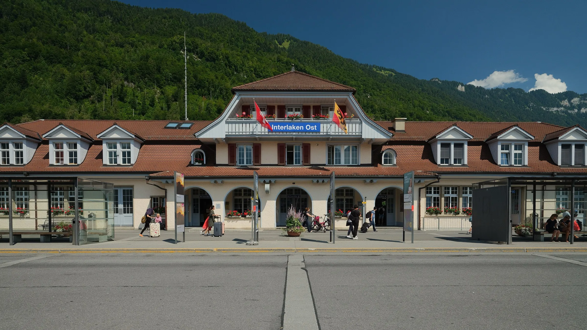 The front of Interlaken Ost station on a sunny day with a wooded hillside behind.