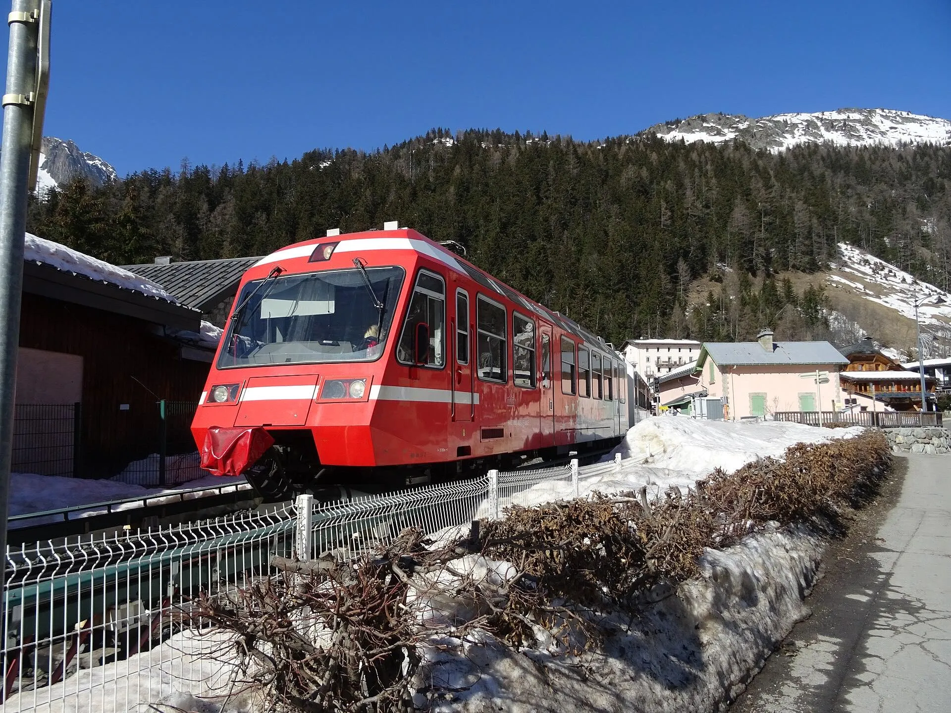 A red TER train passing Montroc-le-Planet with snow on the ground and forested slopes behind.
